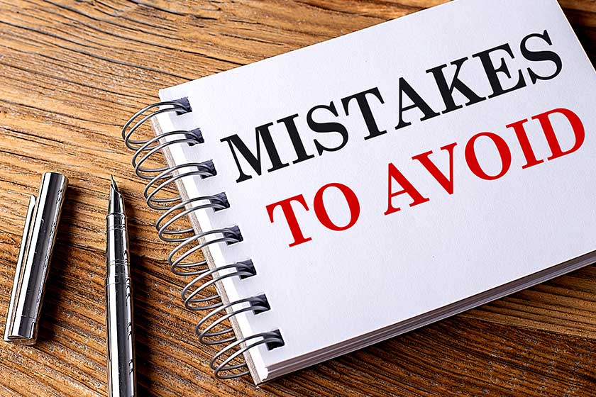 MISTAKES TO AVOID text on a notebook with pen on wooden background